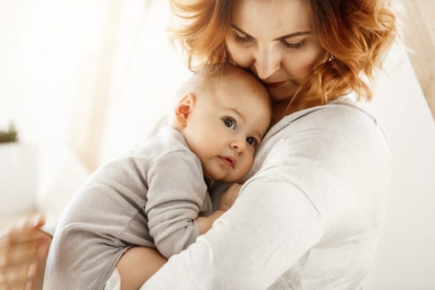 beautiful young mother tenderly hugs her little cute child mom looking her kid smiling while baby looks aside snuggling mom chest happy family moments 176420 12204